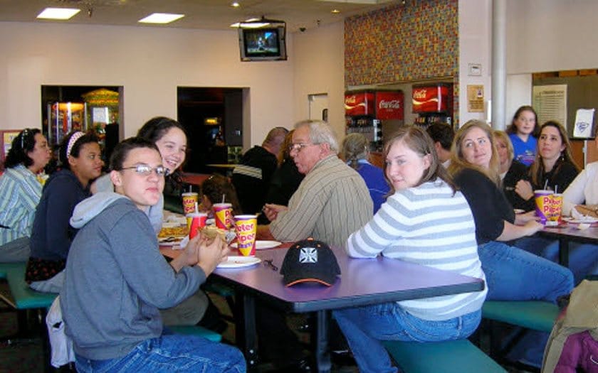 Group of people seated at tables in a casual dining area, eating and conversing, with snacks and beverages visible.