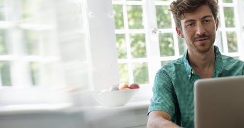 A Connections Academy teacher in a sage green button down shirt is communicating with the Learning Coach by writing a message on his laptop. 