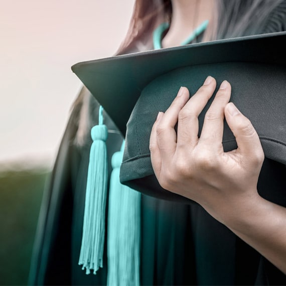 Subject in graduation attire holding the graduation cap with a blue tassel