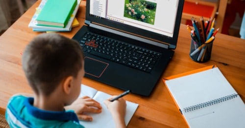 A student in a blue shirt writing on a piece of paper while taking a class at Connections Academy.