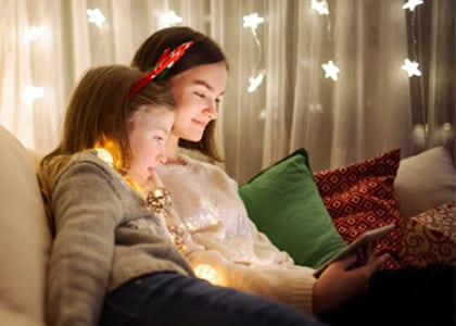 Two young sisters sitting on the sofa working on an online assigment during the holidays for Connections Academy after transferring mid-year.