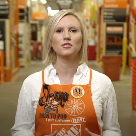 Person wearing an orange apron in a hardware store aisle.