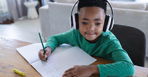 A student wearing a green shirt sitting at the table working on an assignment for Connections Academy.